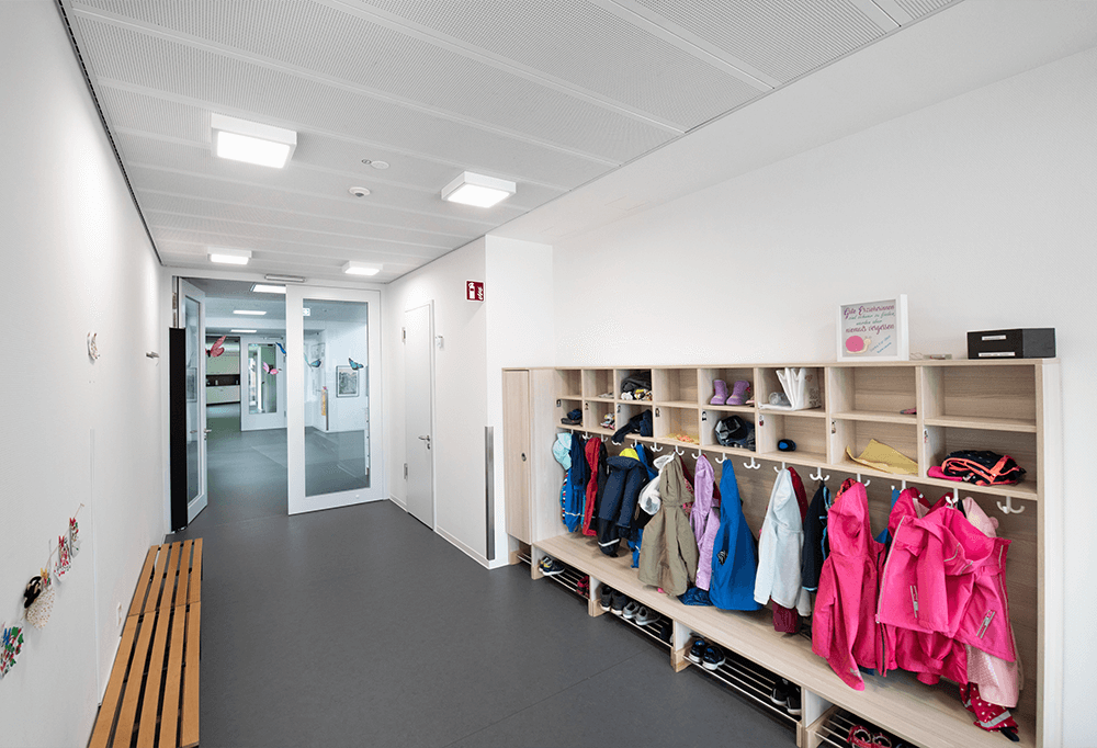 A modern primary school coat hanger room, multiple colourful coats and school bags are hung in a unit
